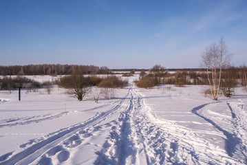 Fototapeta na wymiar Snowy winter road through the snow covered field in countryside