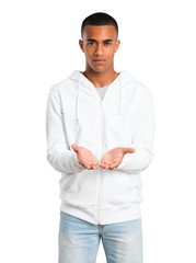 Fototapeta premium Dark-skinned young man with white sweatshirt holding copyspace imaginary on the palm to insert an ad on isolated white background