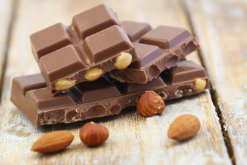 Milk chocolate pieces with whole hazelnuts and almonds on rustic wooden surface

