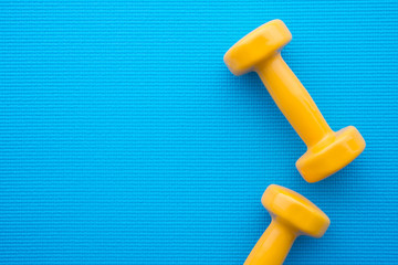 Flat lay of yellow dumbbells for fitness exercise on blue yoga mat background in fitness center - Health care and exercise concept