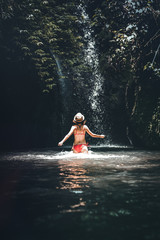 Rear view of Young woman tourist in the deep jungle with waterfall. Real adventure concept. Bali island.