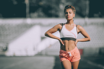 Sexy sport girl posing at stadium. Fitness girl with a sports figure in shorts and tank top in the stadium. Girl after sport day. Grey background