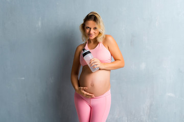 Blonde pregnant woman doing sport with a bottle of water