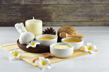 Homemade spa set (body and facial scrub, hair treatment oil, herbal compress, aroma candle and plumeria) in oriental style on white wood and old wood background, body and hair care concept