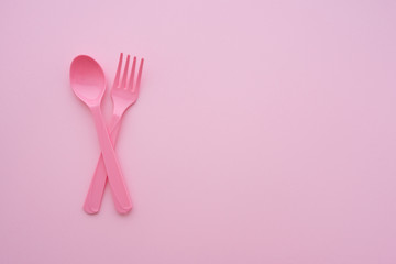 Flat lay of pink pastel spoon and fork on pink background with copy space. Minimal simple color style. Restaurant accessories utensil on table.