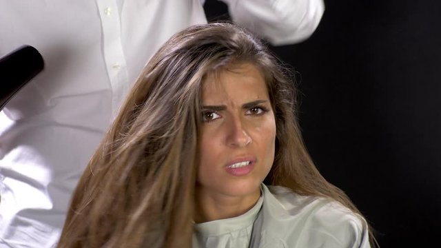 Beautiful female model getting angry with hairdresser drying her long hair strong