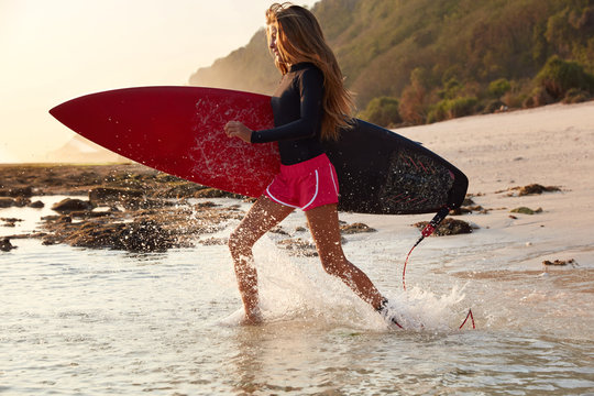 Horizontal shot of active woman likes surfing, cant imagine life without extreme water sport, being in motion, makes splashes from ocean water, recreats in resort country near rocky mountains.