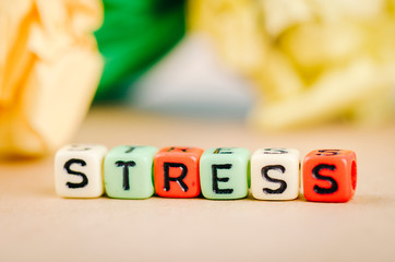Colorful alphabet letter dice text on desk, spelling STRESS over crumple paper background