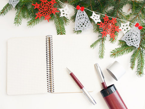 Desktop decorated for new year. Notebook to record a list of Christmas shopping, to do list. Fir branches and garland crocheted, snowflakes and Christmas trees.