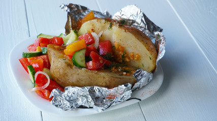 Baked in foil potato with vegetable salad on a wooden table.