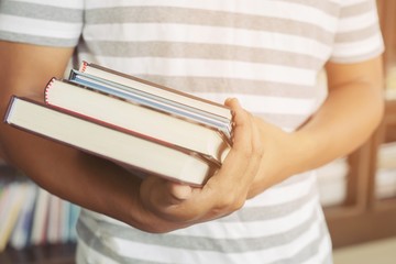 close up student young man hand holding books are placed front bookshelf in a library University. love to read education concept. with filter Tones retro vintage warm effect.