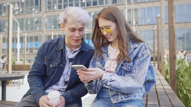Cheerful male and female friends enjoying free time together joking and using smart phone