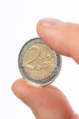 Close-up of caucasian male fingers holding a two Euro coin €2 on a white background.