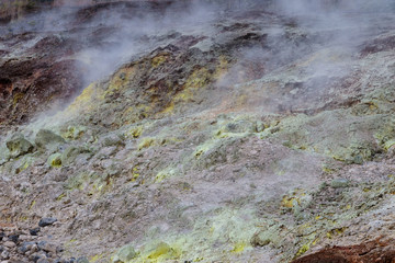 Sulfur Bank in Volcano National Park in Hawaii. Yellow sulfer deposits are on the ground; volcanic gas rise into the air.  