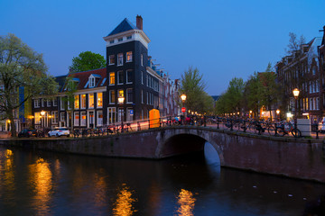 Naklejka premium Houses over canal with glowing lights at night, Amsterdam, Netherlands