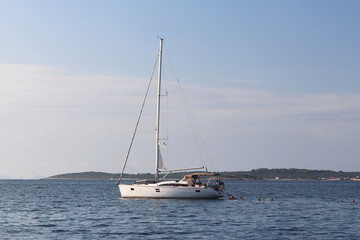 Obraz premium A modern sailing yacht is anchored in a bay. People bathe in the sea. Active rest on the Adriatic Sea of the Mediterranean region. Dalmatian riviera of Croatia. Prestigious and rich lifestyle