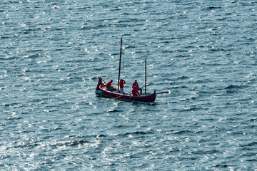 Barca a remi rossa, con persone che osservano in lontananza, in mezzo al mare