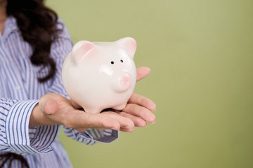 A woman holding a pink piggy bank, copy space next to her.