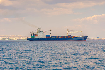 Fototapeta premium the ship is a container ship sailing along the sea, against the background of the coastline on the horizon and the sky covered with clouds