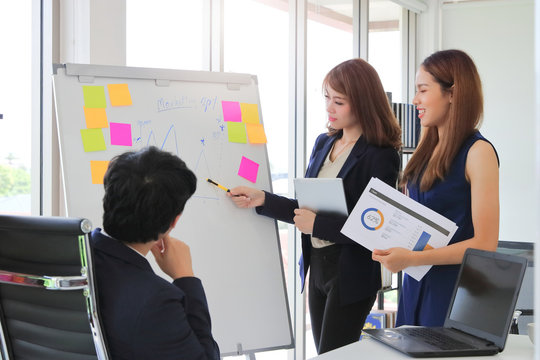 Confident young Asian business woman explaining strategies on flip chart to executive in boardroom
