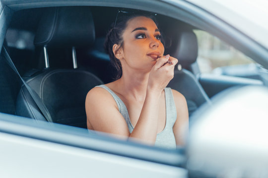 Close up of beautiful woman getting her lips painted while sitting in car.