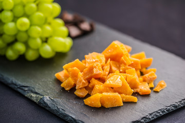 Cheese pieces and juicy grapes on slate board.