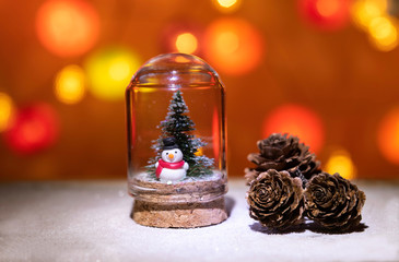 Snow man with Christmas tree in glass tube near pine cone isolated from Christmas light background
