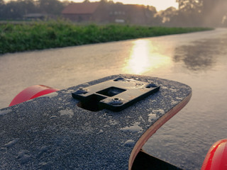 Longboard auf nasser Straße mit Sonnenlicht