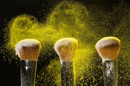 Mineral make up and objects concept - Three make up brushers in yellow dust over dark background