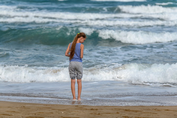 Girl in striped t-shirt and with curly hair looking at the sea
