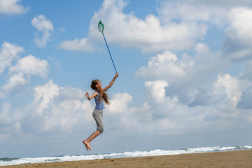 girl in a  in striped t-shirt on the sea catches clouds by a net on a sunny day