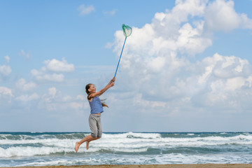 girl in a  in striped t-shirt on the sea catches clouds by a net on a sunny day