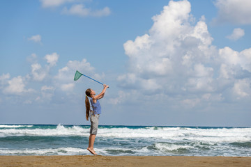 girl in a  in striped t-shirt on the sea catches clouds by a net on a sunny day