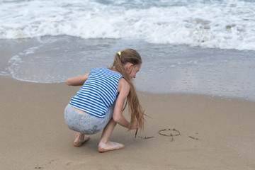 Girl draws a sun in the sand on the beach