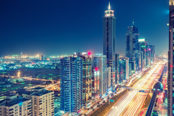 Fototapeta na wymiar Spectacular urban skyline with colourful city illuminations. Aerial view on highways and skyscrapers of Dubai, United Arab Emirates.