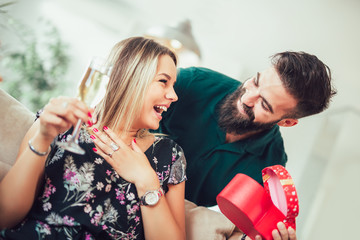 Smiling young man surprising cheerful woman with a gift box at home