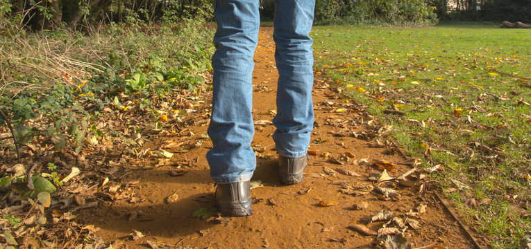 A man in jeans walks along a path covered in fallen leaves during autumn