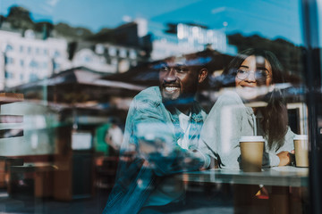 Positive relaxed young couple hugging and smiling while sitting in the cafe and looking into the distance