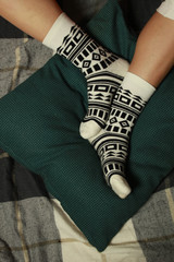 Women's legs in beautiful socks with black geometric authentic ornament. Legs lie on a green pillow.