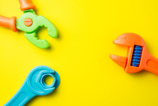 Flat lay of blue nut wrench, orange adjustable wrench and clamp plastic toy on yellow background. Playing with toys can be an enjoyable means of training young children for life in society.