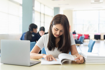Obraz premium Young asian female student college is reading book while sitting on table with laptop.