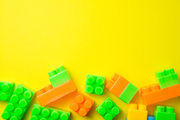 Flat lay of colorful blocks brick plastic toy on yellow background with copy space. Playing with toys can be an enjoyable means of training young children for life in society.