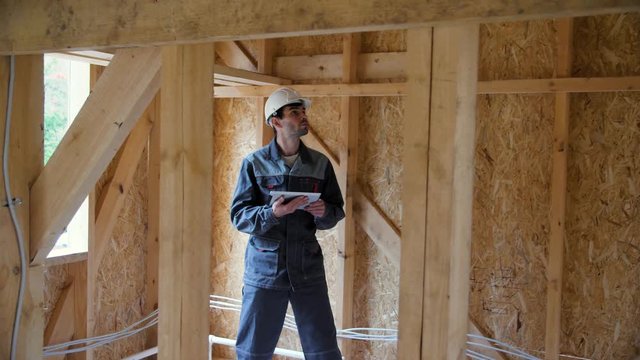 Architect or builder check plans in a half built timber frame house. Engineer on the construction of a frame wooden house. 4k 60fps slow motion