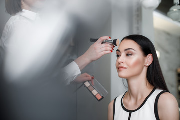 Makeup artist emphasizing cheekbones while using dark and light colors for pretty woman