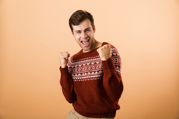 Image of happy man 20s with stubble wearing knitted sweater screaming and clenching fists, isolated...