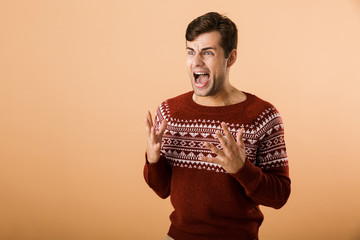 Image of caucasian man 20s with stubble wearing knitted sweater screaming and expressing outrage,...