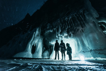 Surreal landscape with people exploring mysterious ice grotto cave. Outdoor adventure. Family exploring huge icy cave, dark majestic landscape. Magical silhouettes on background of illuminated ice.