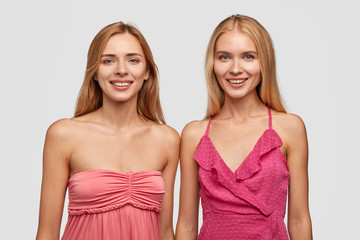 Fahionable light haired women pose for fashion magazine, dressed in pink dresses, have happy...