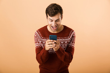 Image of unshaved man 20s with stubble wearing knitted sweater using mobile phone, isolated over...