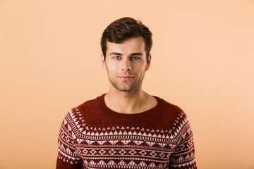 Fototapeta premium Image of happy man 20s with bristle wearing knitted sweater smiling at camera, isolated over beige background